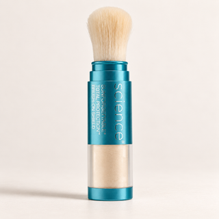A single makeup stick with a teal metallic body, clear lower section showing beige powder, and a soft cream-colored brush on top, photographed against a clean off-white background.