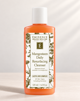 A bottle of Eminence Organic Skin Care Mangosteen Daily Resurfacing Cleanser, featuring an orange liquid inside a translucent bottle with a white cap and a white botanical label.
